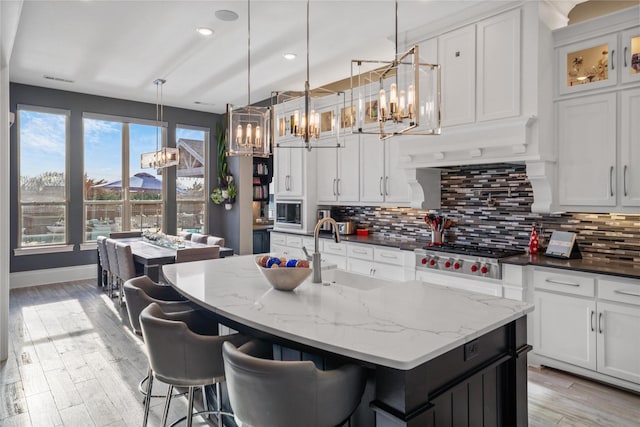 kitchen featuring light wood finished floors, white cabinets, decorative backsplash, stainless steel gas stovetop, and a sink