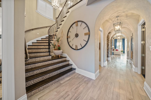 foyer entrance featuring baseboards, arched walkways, a notable chandelier, and wood finished floors