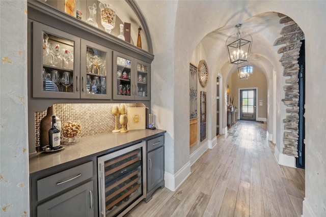 bar with a dry bar, beverage cooler, arched walkways, baseboards, and light wood-type flooring