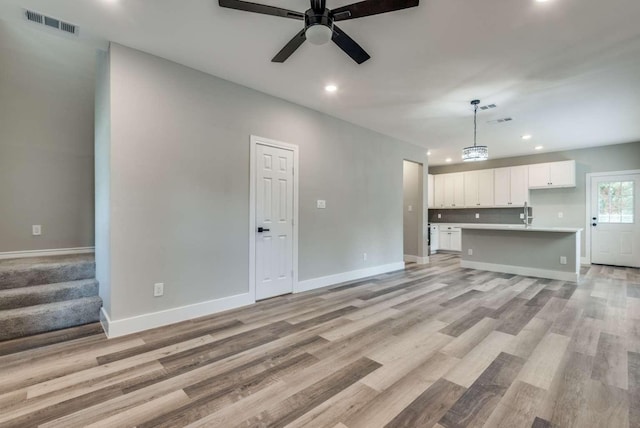 unfurnished living room featuring recessed lighting, stairway, light wood-type flooring, and baseboards