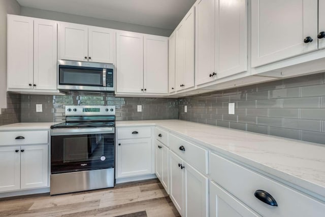 kitchen featuring stainless steel appliances, backsplash, white cabinets, light stone countertops, and light wood-type flooring