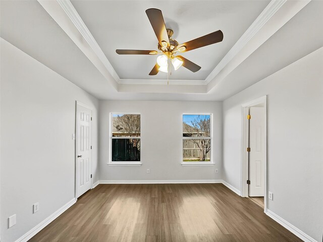 empty room featuring dark wood-style floors, a raised ceiling, ornamental molding, a ceiling fan, and baseboards