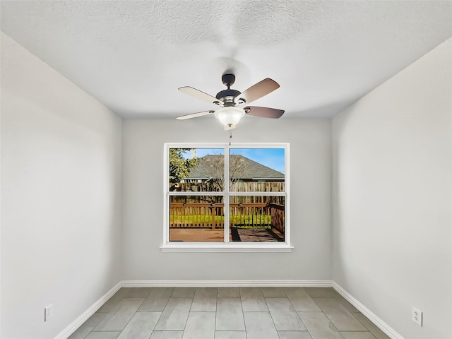 spare room with ceiling fan, a textured ceiling, and baseboards