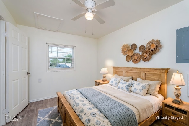 bedroom with wood finished floors, a ceiling fan, baseboards, electric panel, and attic access