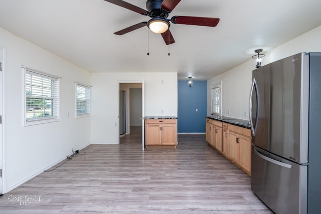 kitchen featuring light wood finished floors, dark countertops, freestanding refrigerator, light brown cabinets, and baseboards