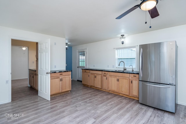 kitchen with a sink, a ceiling fan, light wood-type flooring, freestanding refrigerator, and dark countertops