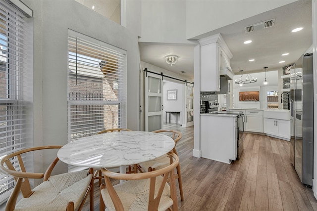 kitchen with a barn door, range with electric cooktop, a sink, visible vents, and light wood-type flooring