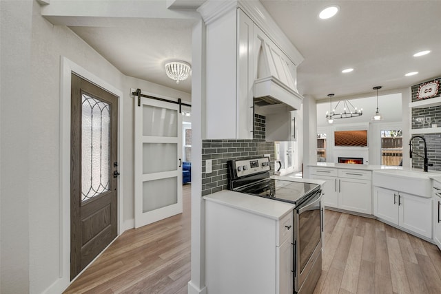 kitchen with a barn door, a sink, light wood finished floors, and stainless steel electric stove