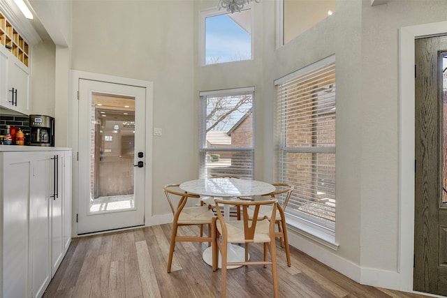 dining area with light wood-style floors, a high ceiling, and baseboards