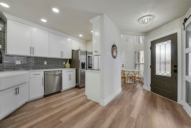 kitchen featuring appliances with stainless steel finishes, light countertops, light wood-style floors, white cabinetry, and backsplash