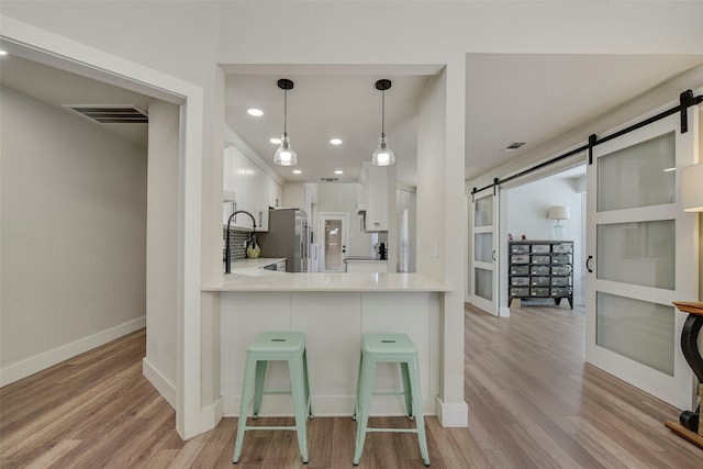 kitchen featuring visible vents, a barn door, light wood-style floors, freestanding refrigerator, and white cabinets