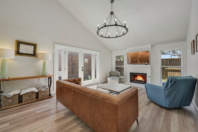 living area featuring light wood-style floors, a lit fireplace, high vaulted ceiling, and french doors