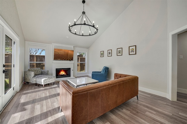 living room featuring baseboards, a chandelier, wood finished floors, a lit fireplace, and high vaulted ceiling