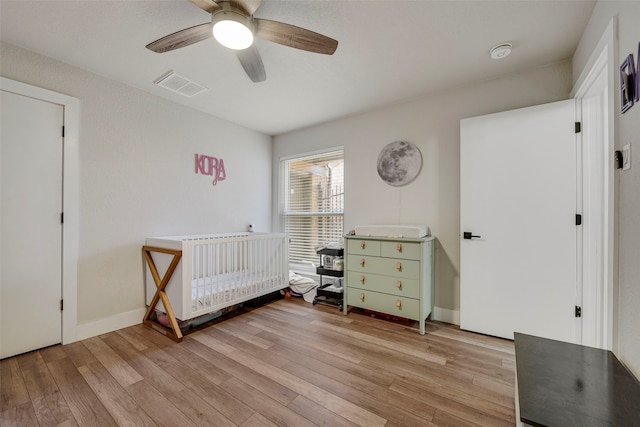 bedroom featuring a crib, visible vents, baseboards, ceiling fan, and light wood-style floors