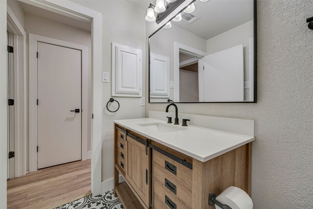 bathroom with visible vents, a textured wall, vanity, wood finished floors, and baseboards