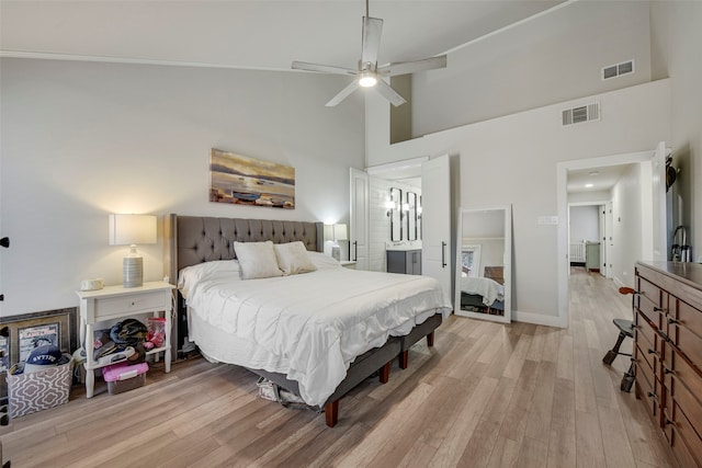 bedroom featuring baseboards, visible vents, a towering ceiling, and light wood finished floors