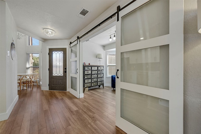 foyer with a barn door, hardwood / wood-style flooring, visible vents, and a healthy amount of sunlight