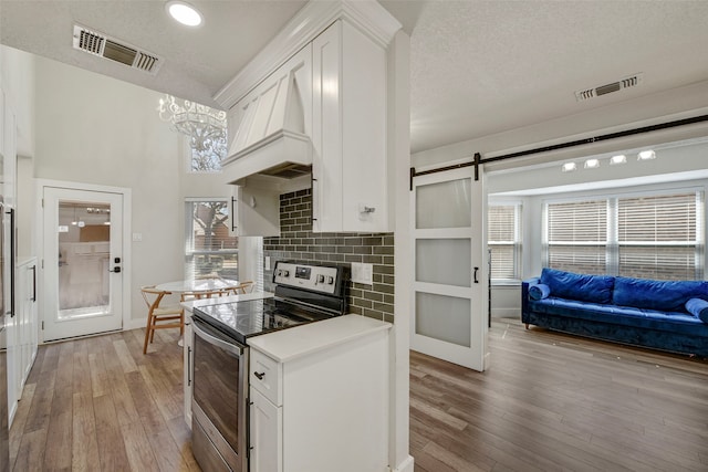 kitchen with electric range, a barn door, light wood-type flooring, and visible vents