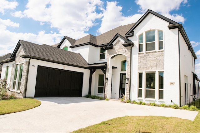 french country home with roof with shingles, brick siding, a garage, stone siding, and driveway