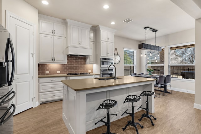 kitchen with premium range hood, a sink, visible vents, appliances with stainless steel finishes, and backsplash