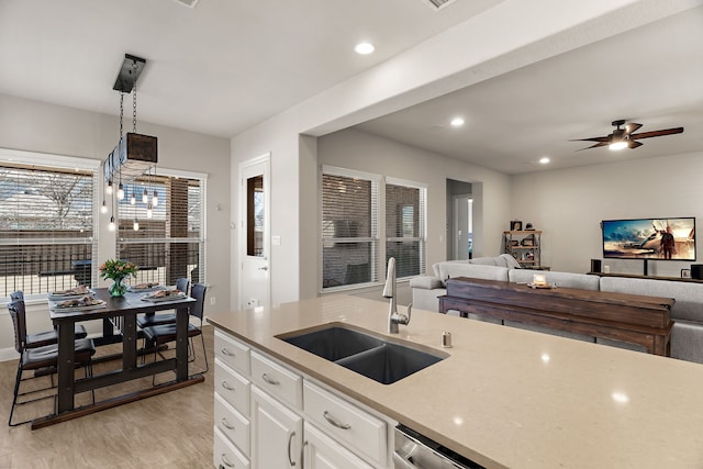 kitchen featuring light stone counters, hanging light fixtures, open floor plan, white cabinetry, and a sink