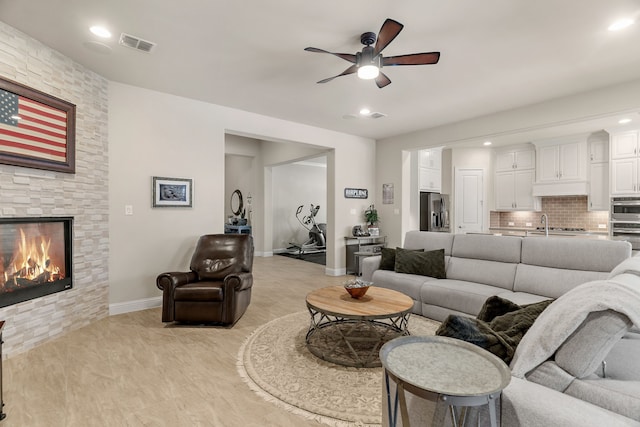 living room with visible vents, baseboards, ceiling fan, a stone fireplace, and recessed lighting