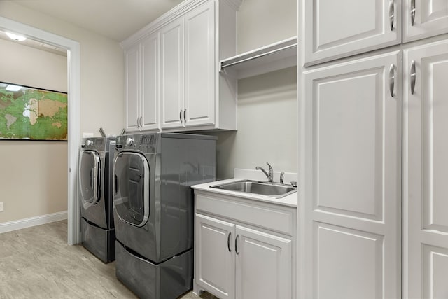 clothes washing area with cabinet space, baseboards, washer and clothes dryer, and a sink