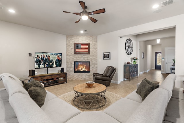 living area featuring light wood-style floors, visible vents, and a stone fireplace