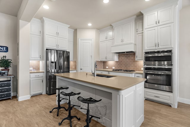 kitchen featuring a sink, white cabinetry, appliances with stainless steel finishes, a kitchen bar, and custom range hood