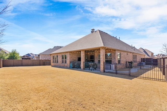 back of house with brick siding, a fenced backyard, roof with shingles, and a patio