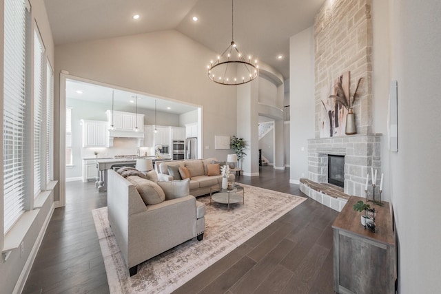 living room featuring a chandelier, high vaulted ceiling, a stone fireplace, and dark wood-type flooring