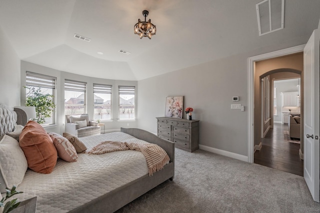 carpeted bedroom with arched walkways, visible vents, and baseboards