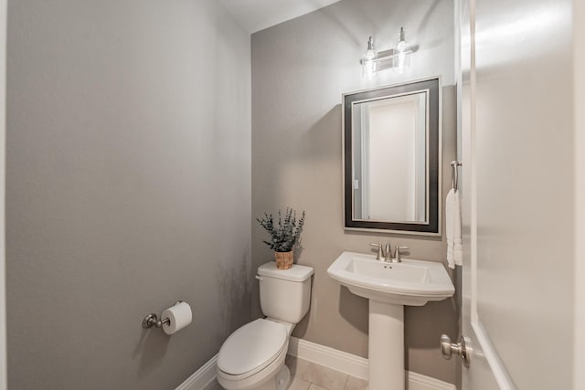 half bath with toilet, baseboards, a sink, and tile patterned floors