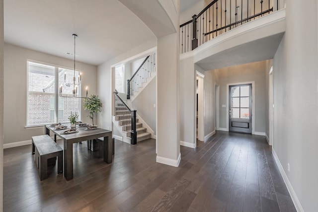 dining area featuring dark wood-type flooring, a notable chandelier, baseboards, and stairs