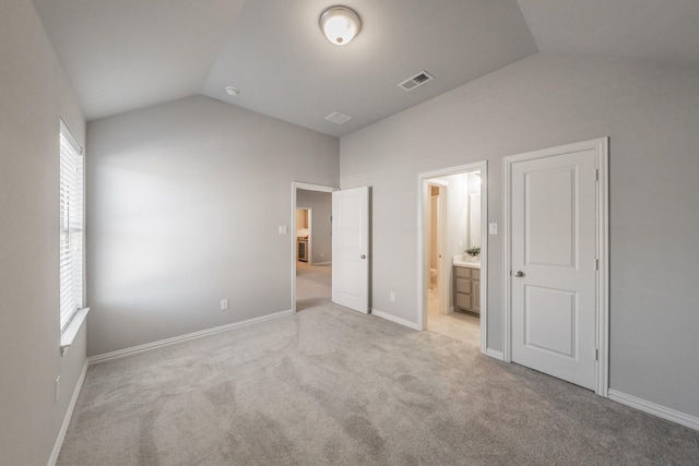 unfurnished bedroom featuring lofted ceiling, visible vents, light carpet, ensuite bath, and baseboards