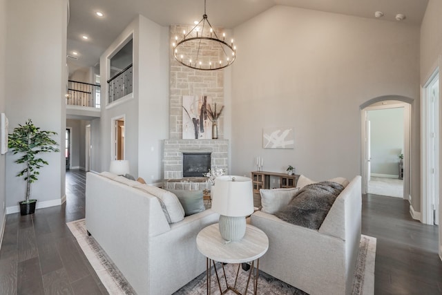 living area featuring arched walkways, dark wood finished floors, a stone fireplace, high vaulted ceiling, and baseboards