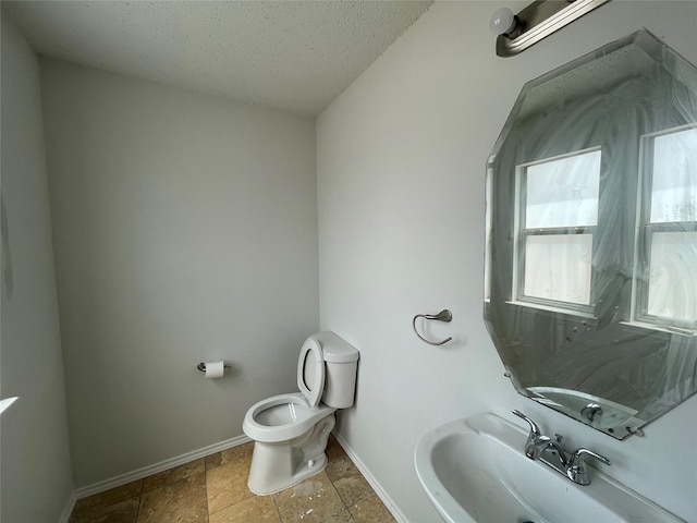 half bath featuring toilet, stone finish floor, a sink, a textured ceiling, and baseboards