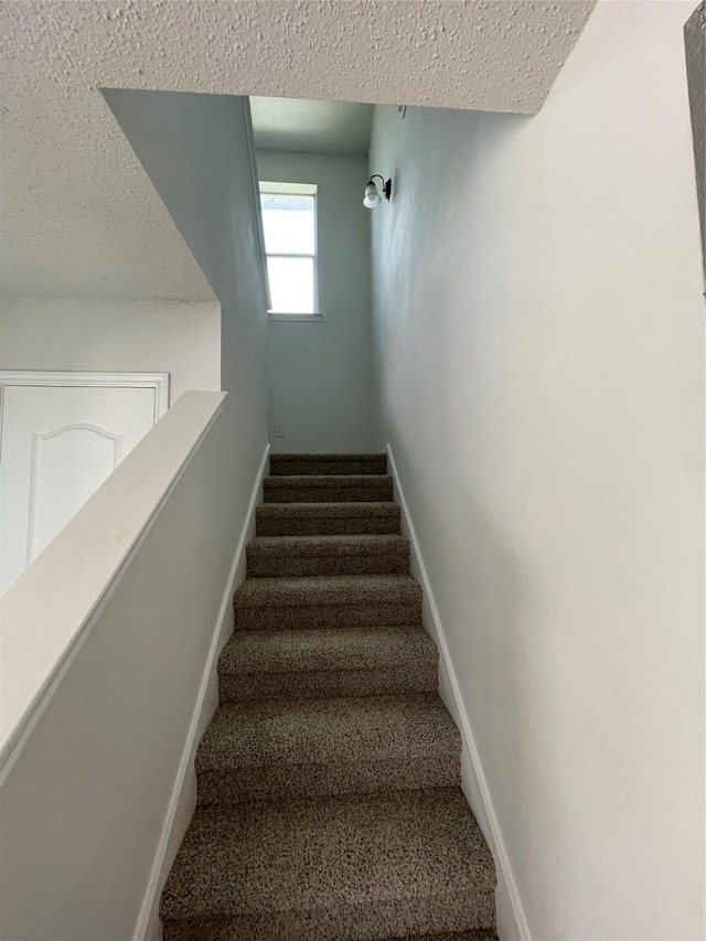 stairs featuring carpet, baseboards, and a textured ceiling