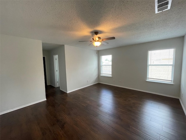 empty room featuring ceiling fan, dark wood-type flooring, visible vents, and baseboards