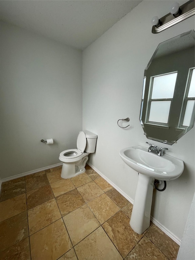 bathroom featuring toilet, baseboards, and a sink