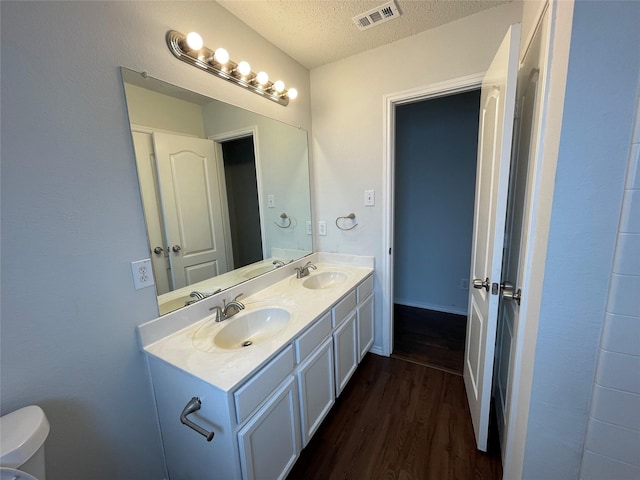 bathroom with a textured ceiling, visible vents, a sink, and wood finished floors