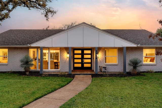 view of front of property with a shingled roof, brick siding, and a yard