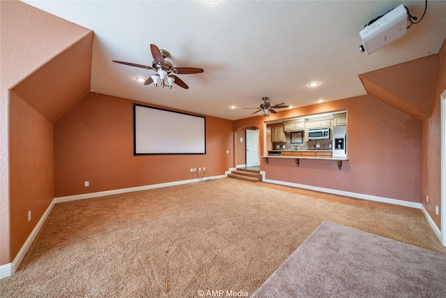 home theater room with lofted ceiling, baseboards, light carpet, and arched walkways