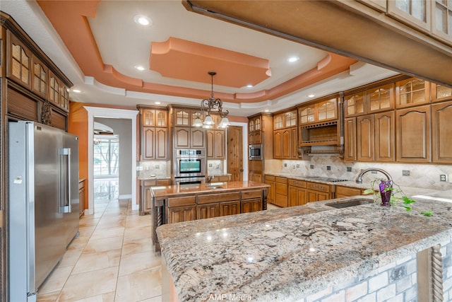 kitchen featuring a sink, appliances with stainless steel finishes, backsplash, a tray ceiling, and brown cabinetry