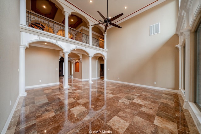 empty room featuring arched walkways, ornate columns, visible vents, ceiling fan, and baseboards