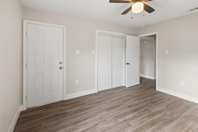 unfurnished bedroom with a closet, visible vents, baseboards, and wood finished floors