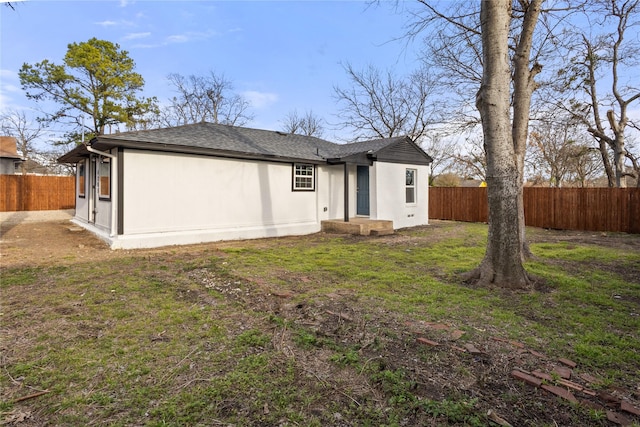 rear view of property with a yard, a shingled roof, a fenced backyard, and stucco siding