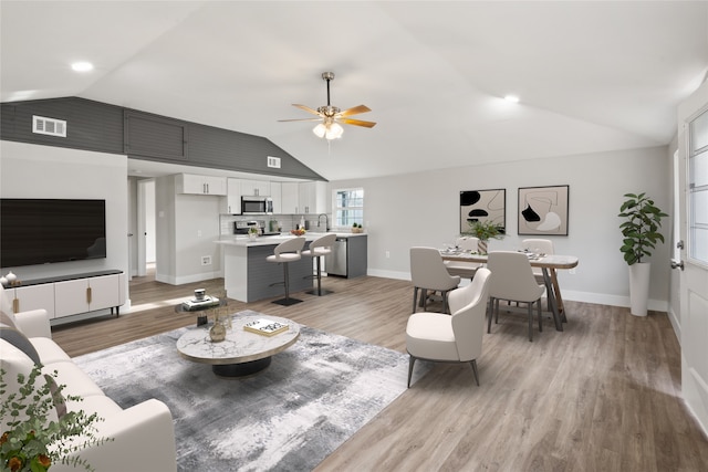 living area featuring ceiling fan, visible vents, baseboards, vaulted ceiling, and light wood-style floors