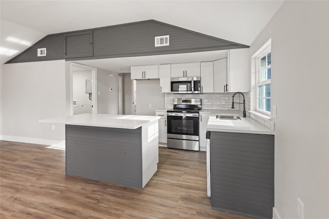 kitchen featuring light countertops, backsplash, appliances with stainless steel finishes, vaulted ceiling, and a sink