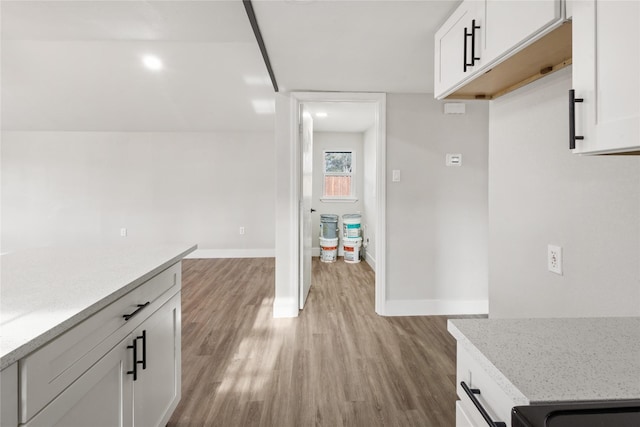 kitchen with baseboards, light stone counters, white cabinets, and light wood-style floors